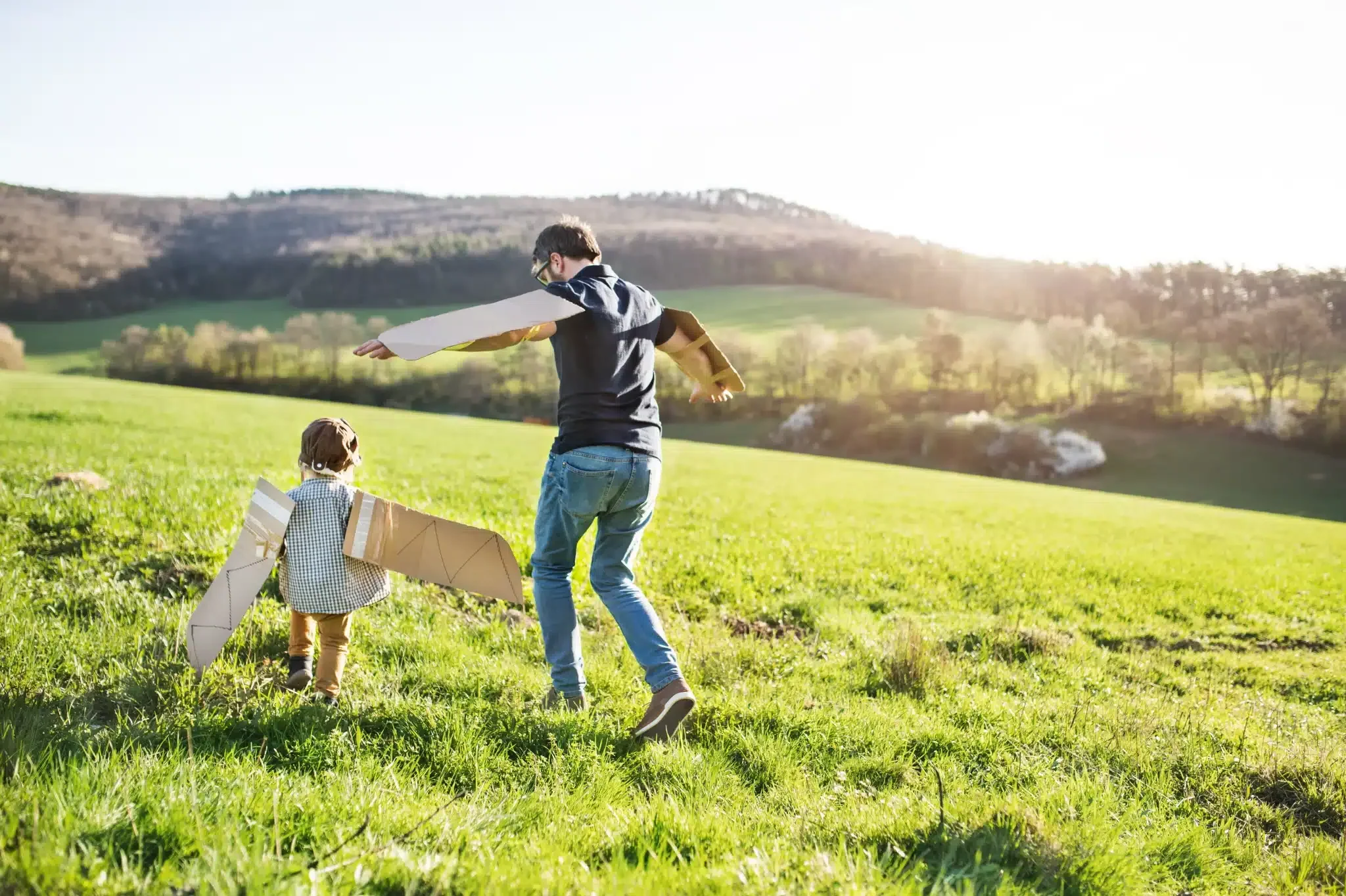 Adult and child playing outside in a sunny field, representing year-round family activities where lice questions can come up.