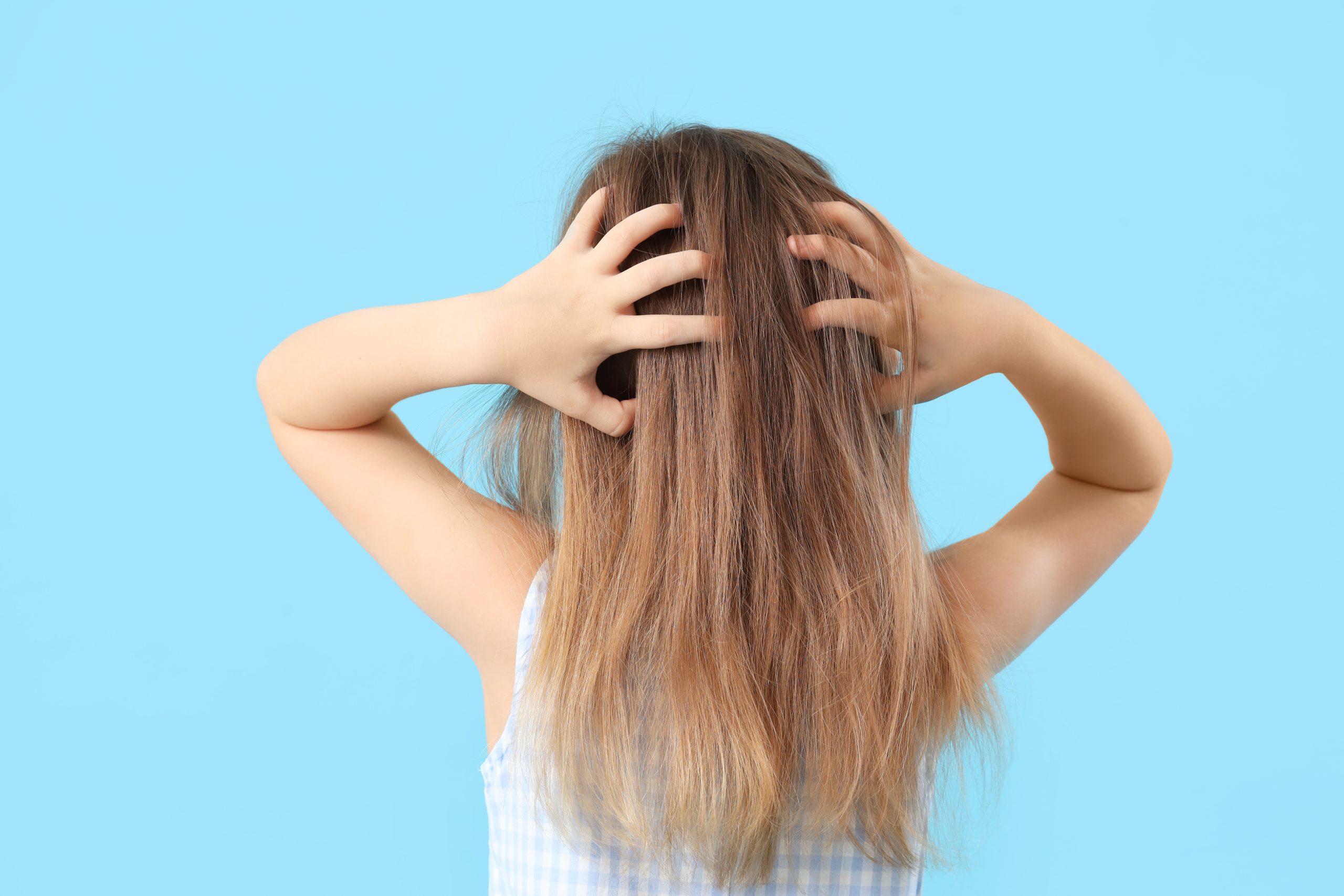 Young girl scratching the back of her head, the kind of first sign parents may notice before checking for lice.