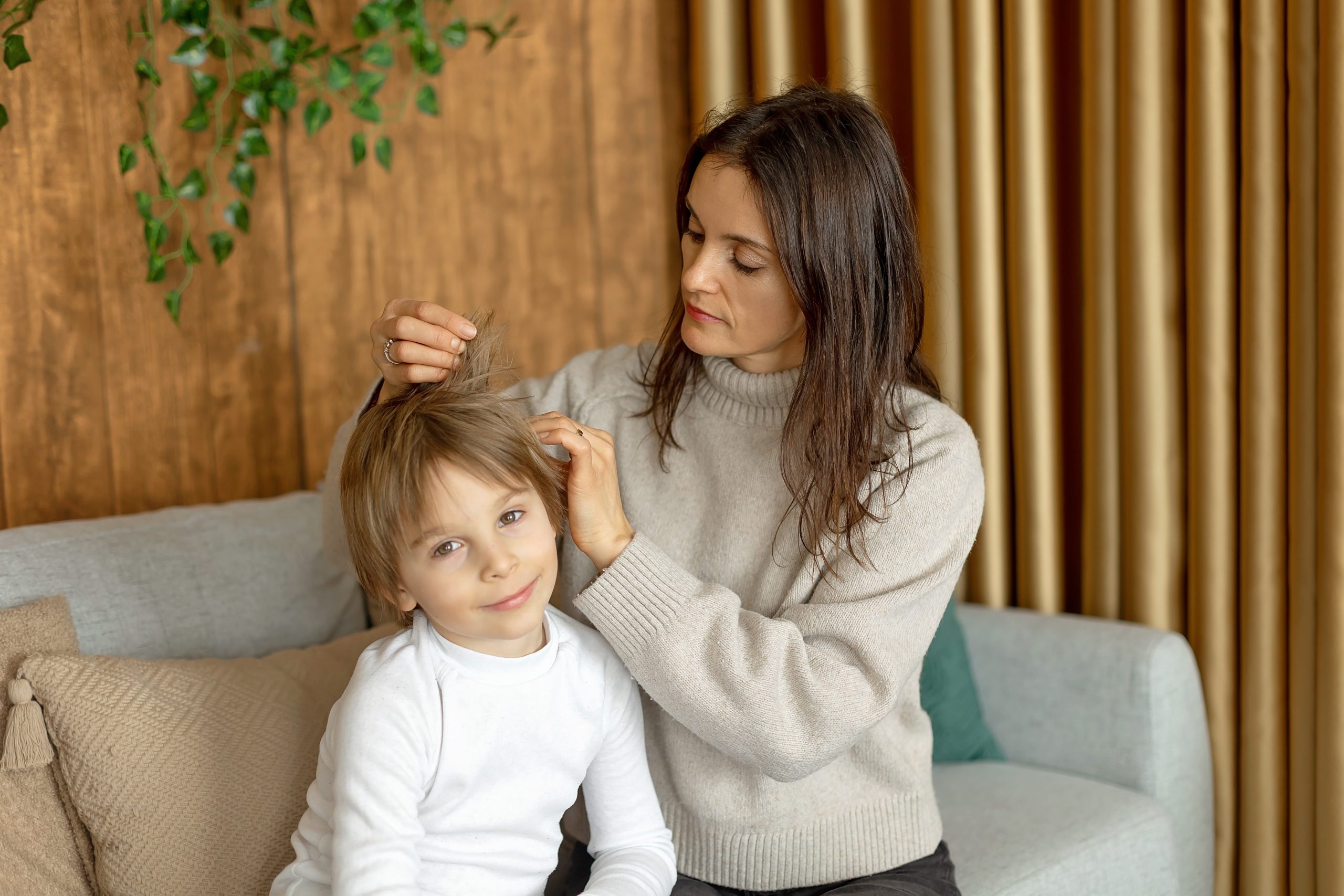 Parent gently parting a child's hair near the scalp under bright daylight to inspect for nits versus dandruff flakes, illustrating the at-home identification check.