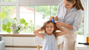Stainless steel nit comb being pulled through a child's conditioned wet hair, with teeth close together