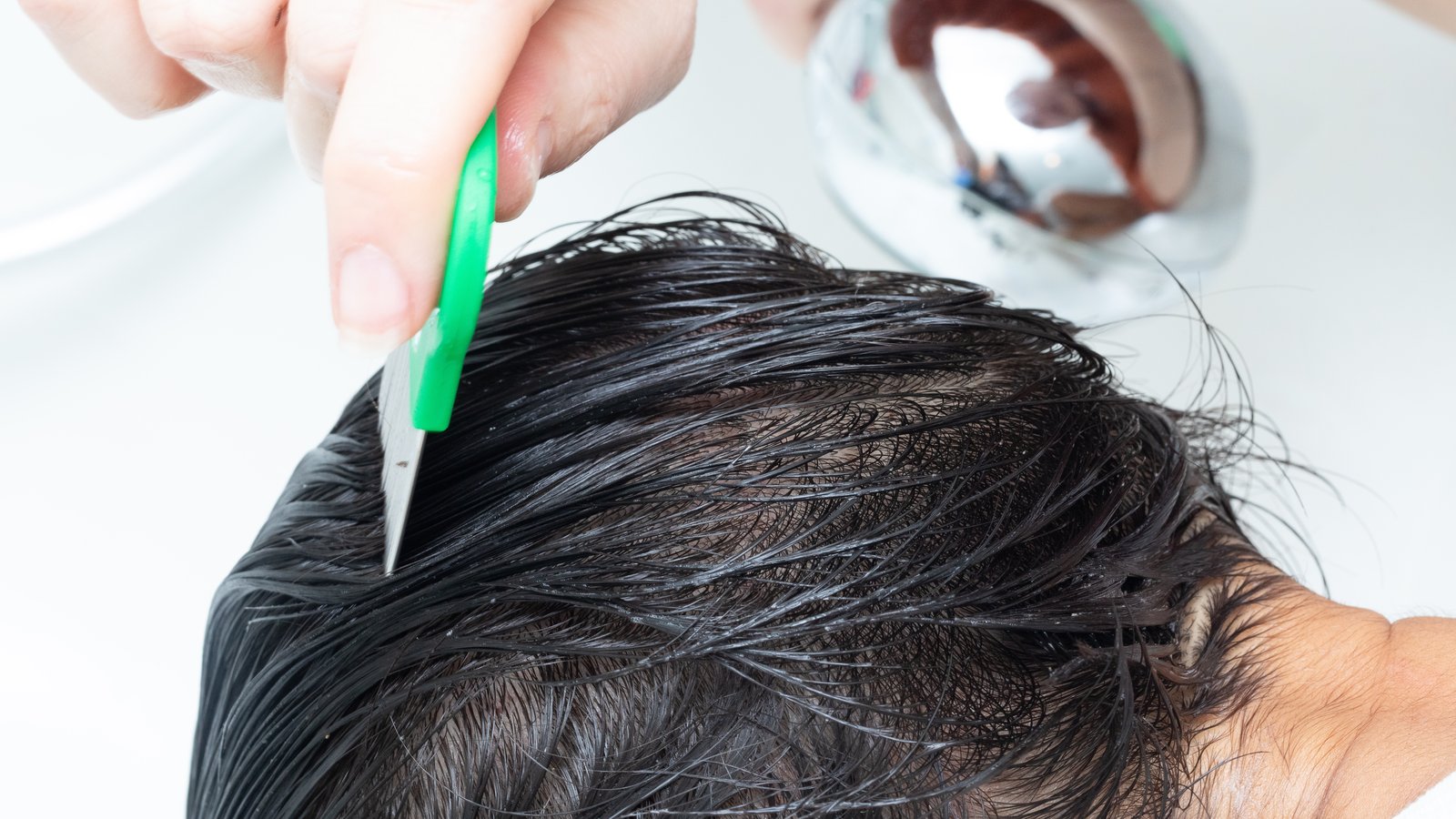 Close-up of a professional using a fine-tooth lice comb on a child's wet hair during a head lice treatment