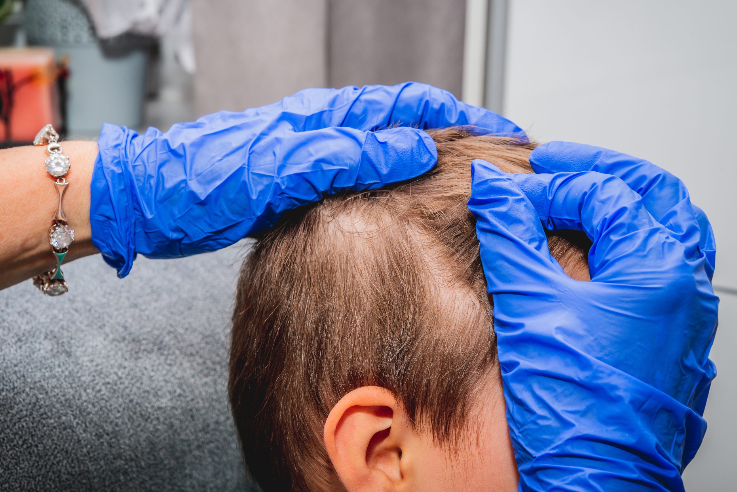 Gloved hands parting a young child's hair behind the ear to inspect the scalp