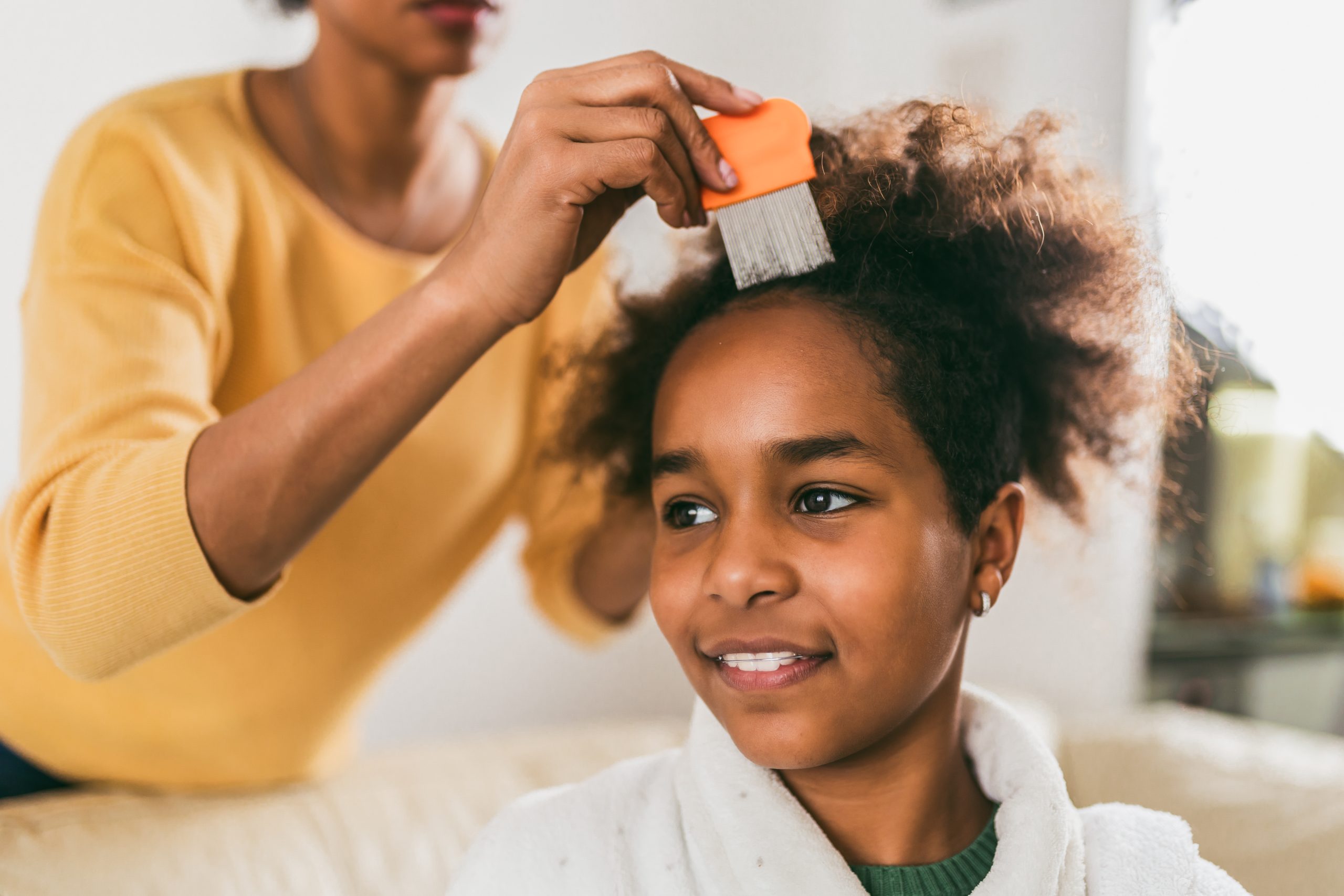 Mother drawing a metal nit comb through her daughter's curly hair at home