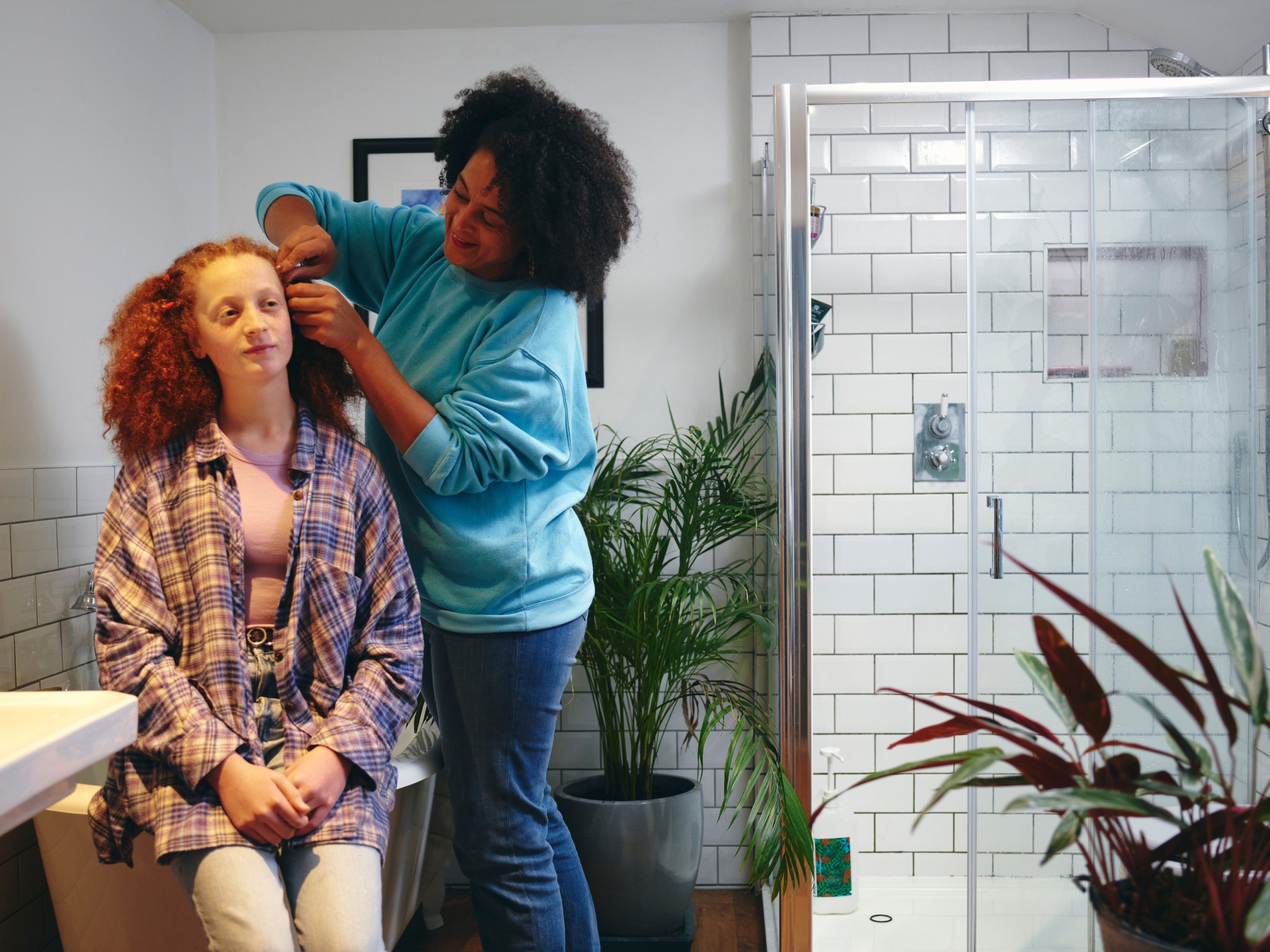 Parent working through a seated child's long curly hair in a home bathroom