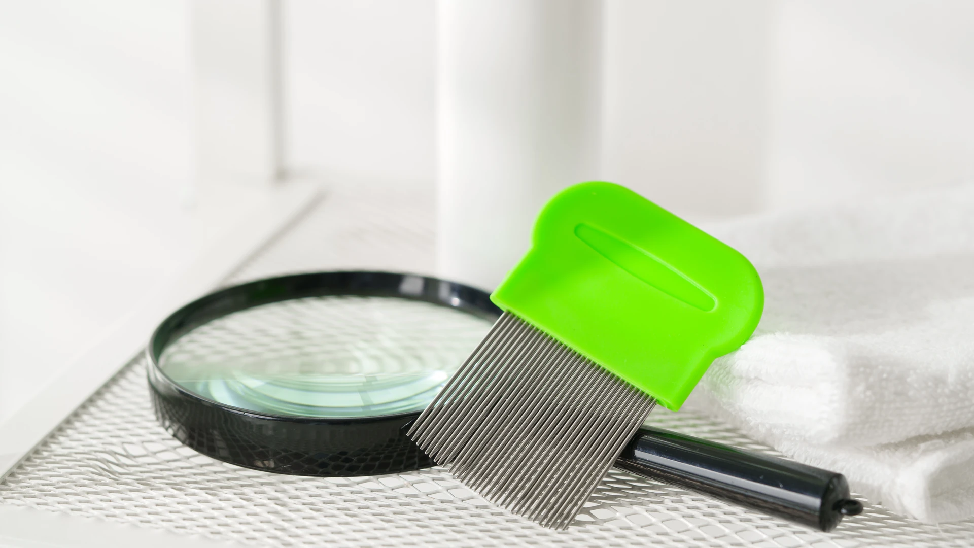 Green-handled fine-tooth comb beside a magnifying glass and folded towel.
