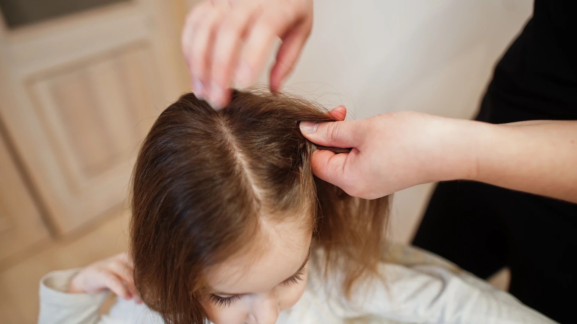 Hands parting a child's hair along the scalp.