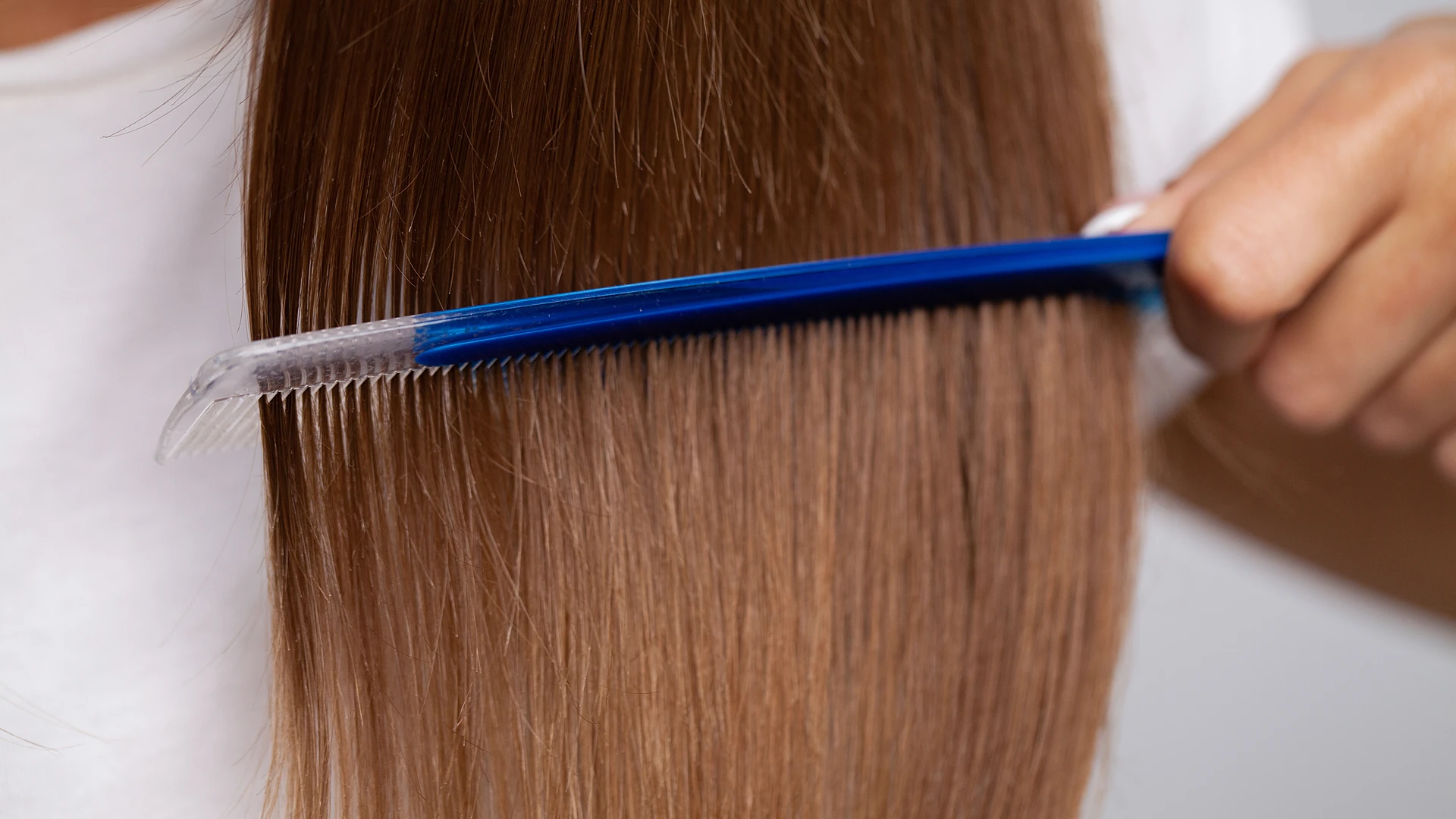 Blue fine-tooth comb drawn through long straight brown hair.